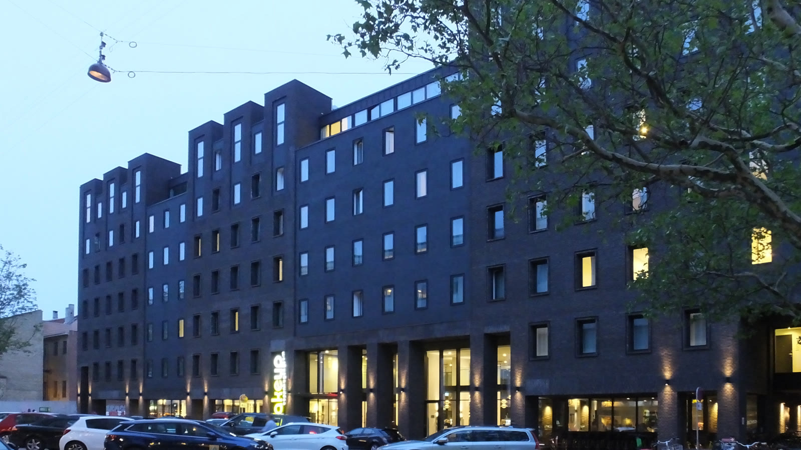 Wakeup Copenhagens mørke facade med oplyste vinduer i skumringen